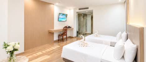 Habitación de hotel con dos camas, piso de madera, televisor, ducha y teléfono.