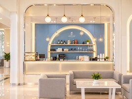 Interior moderno de una cafetería con una pared azul de acento, una barra con diversas bebidas y aperitivos, y diferentes disposiciones de asientos.