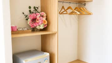 A compact room with a built-in wardrobe, a small refrigerator, and a hanging clothes rack.
