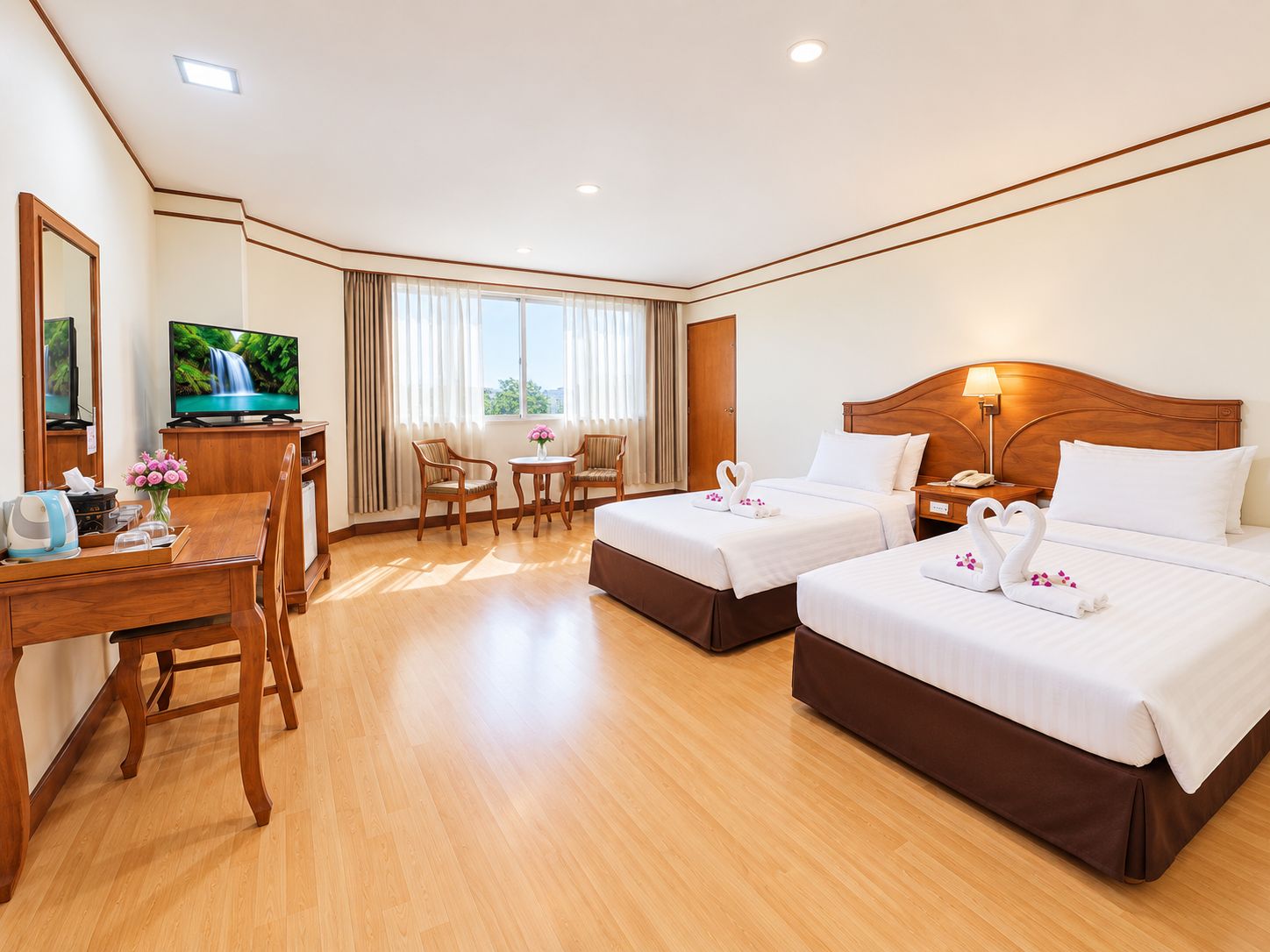 Habitación de hotel con dos camas, un escritorio con televisor, zona de comedor y vistas a zonas verdes.