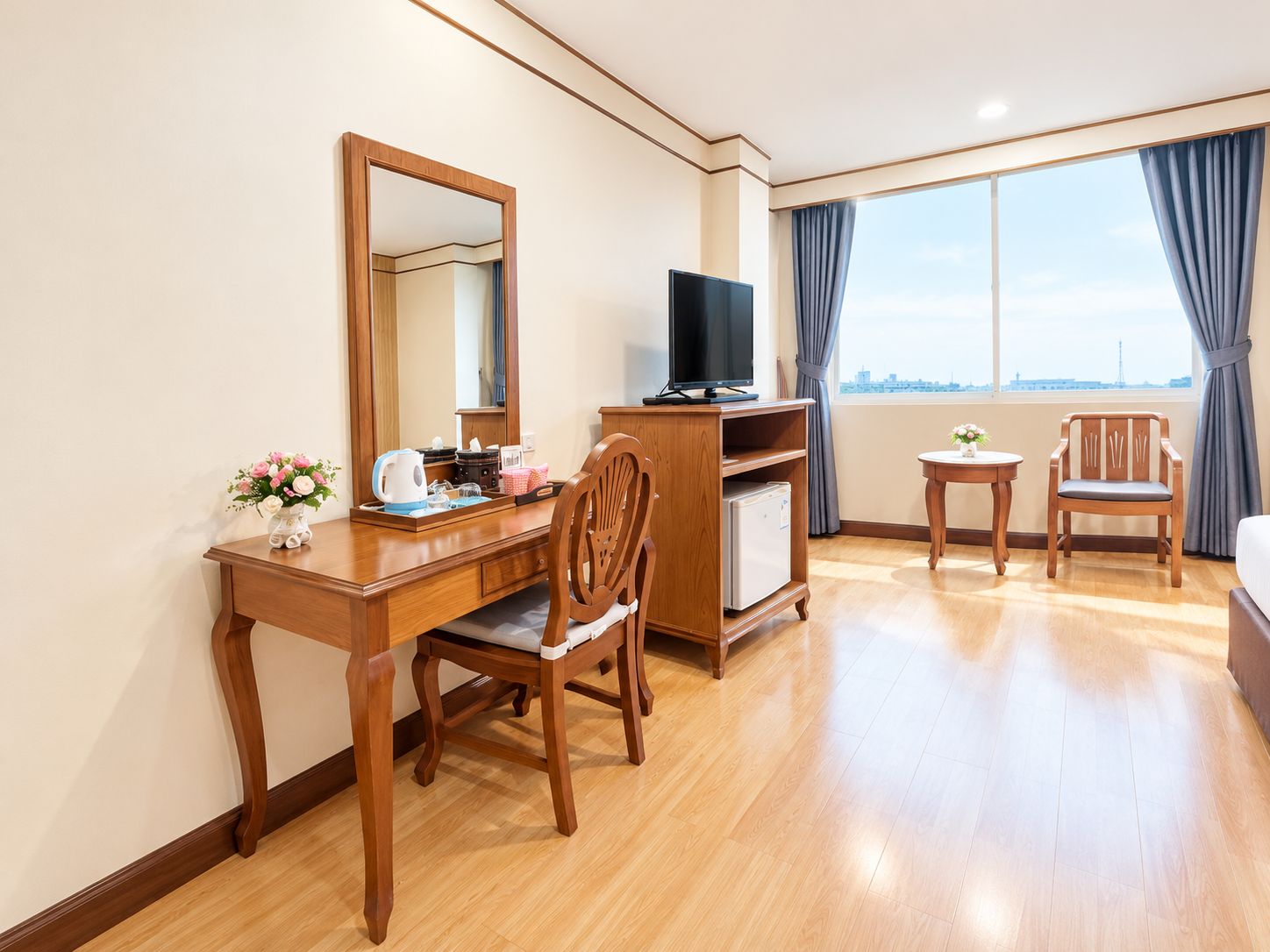Habitación de hotel con un escritorio de madera, una televisión, una mesita con una silla y vistas a la ciudad desde la ventana.