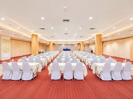 A large conference room with rows of tables and chairs, equipped with water bottles and glasses.