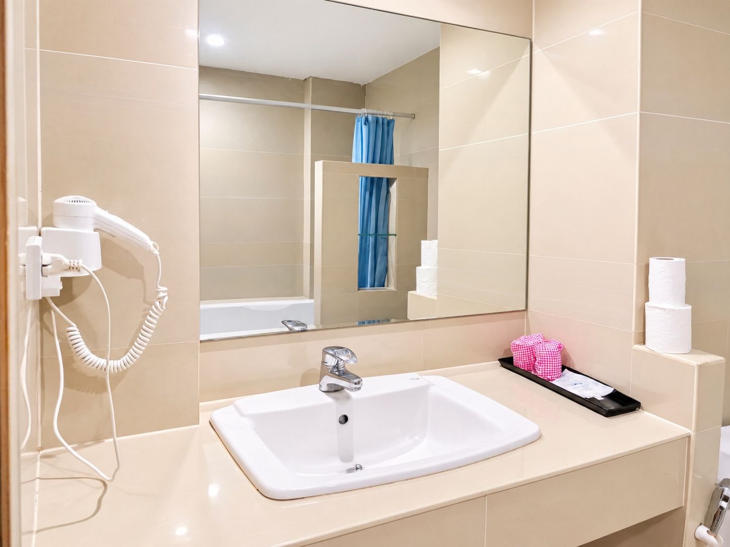 Un bagno con lavandino bianco, uno specchio, un asciugacapelli e un portascopevoli.