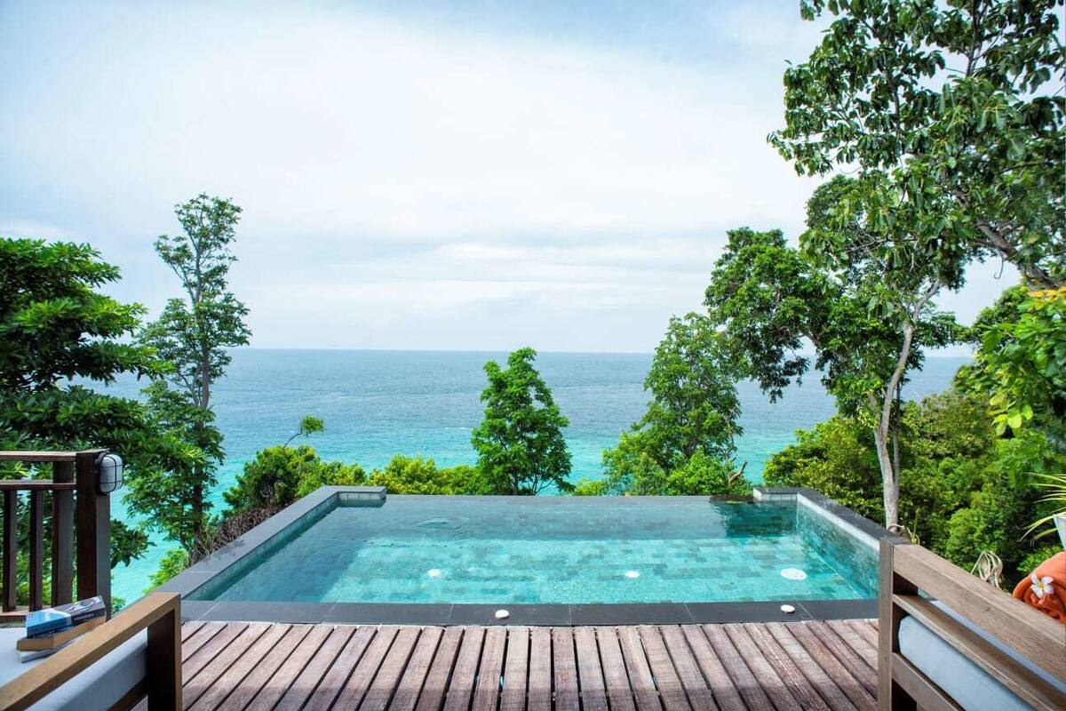A hot tub overlooking a turquoise sea with a wooden deck and lush greenery.