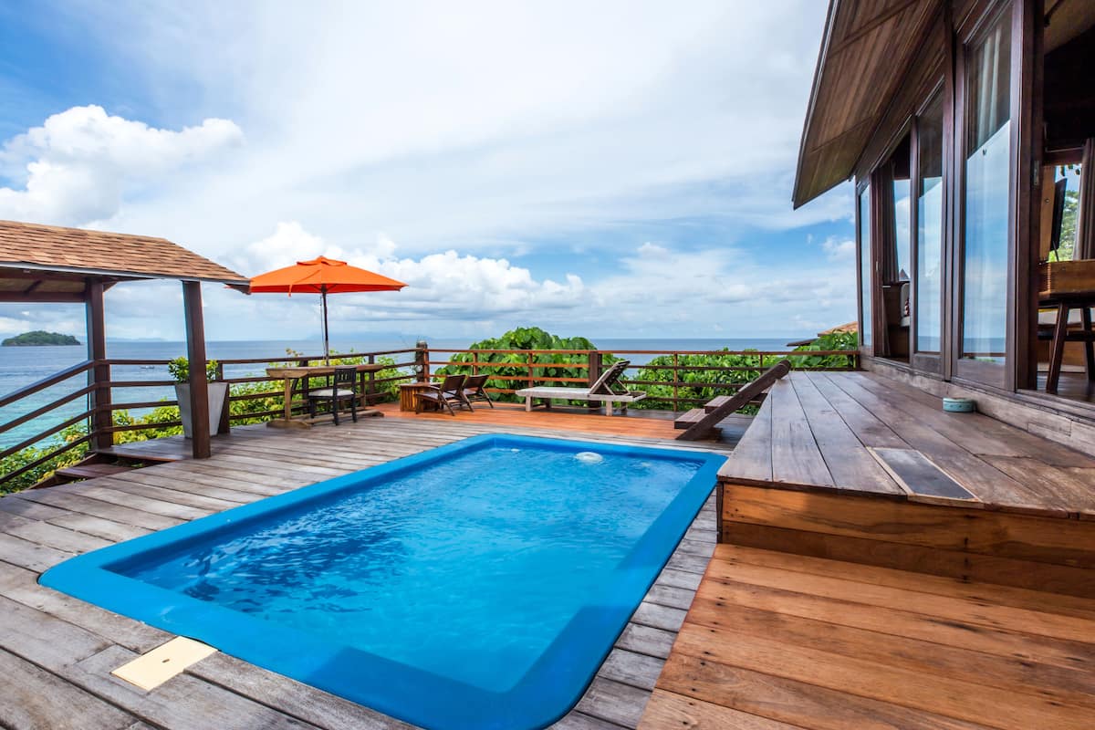 A wooden deck with a swimming pool, outdoor furniture, and a view of the ocean.