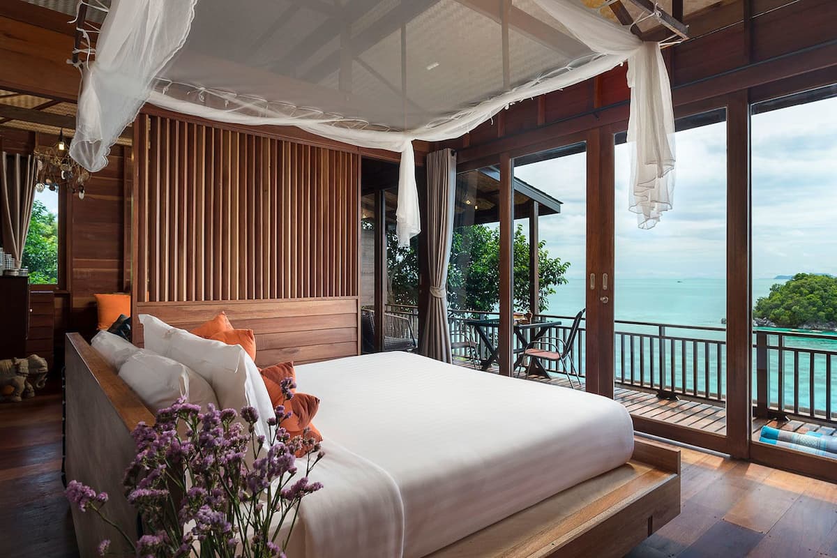 A bedroom with a large bed, wooden paneling, and a view of the sea.