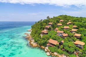 A coastal resort with multiple bungalow-style buildings surrounded by lush greenery and overlooking turquoise waters.