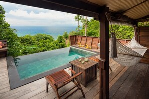Une terrasse en bois dotée d’une piscine à débordement dont le fond est en verre, de meubles en bois et d’un hamac.