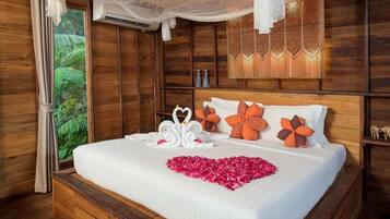 A wooden room with a bed, decorative pillows, a heart-shaped flower arrangement, and a canopy.