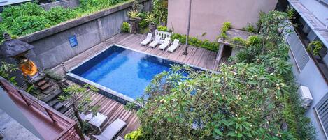 A rooftop pool area with lounge chairs, surrounded by greenery and a small waterfall feature.