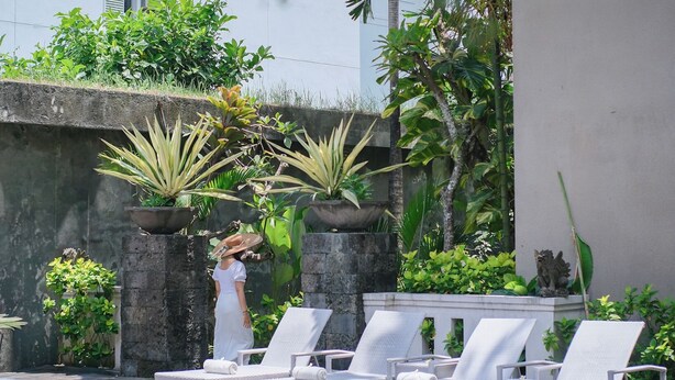 A pool area with white lounge chairs and potted plants. - Kamini Legian Hotel (Kuta)