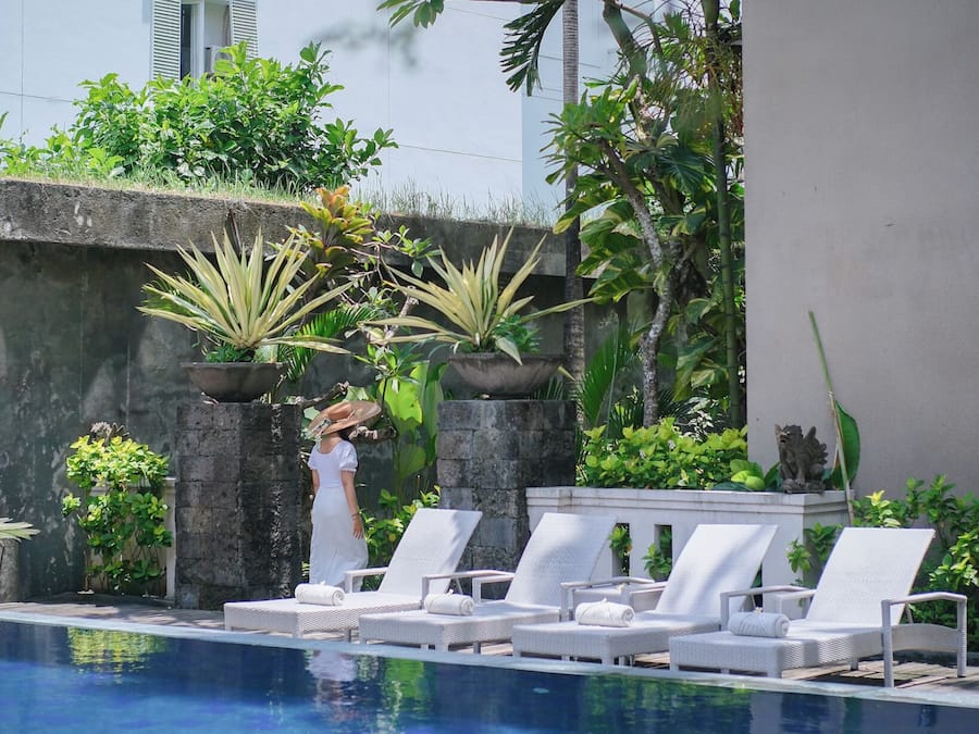 Uma área de piscina com espreguiçadeiras brancas e plantas em vasos.