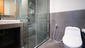 A modern bathroom with a glass shower enclosure, a white toilet, and a sink with a mirror above it. - Kamini Legian Hotel (Kuta)