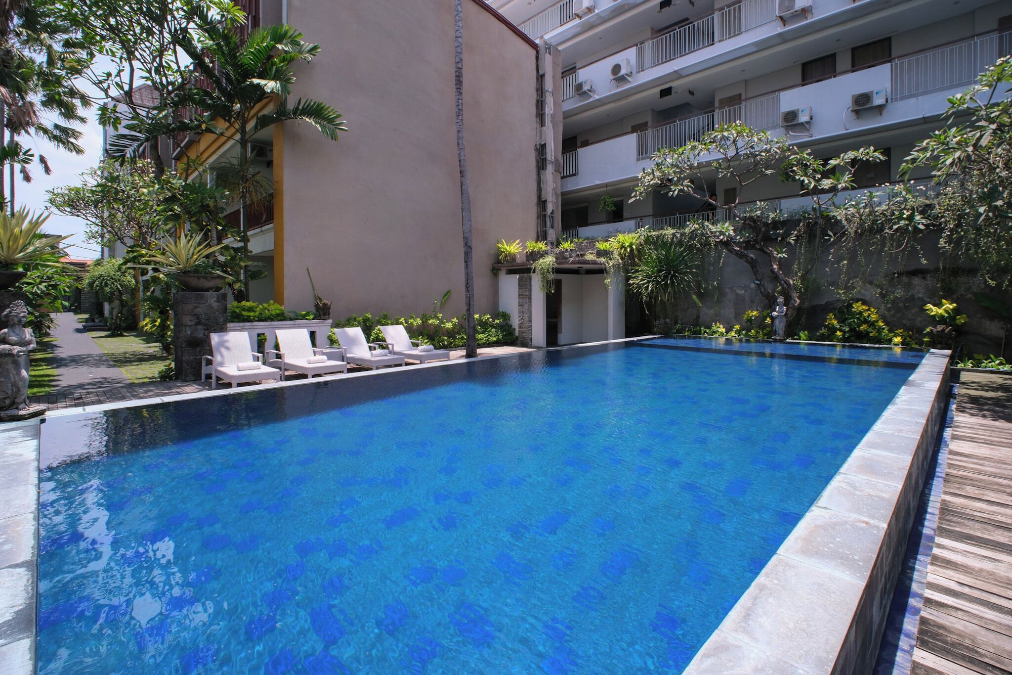 Una piscina con sillas de descanso blancas y plantas tropicales.