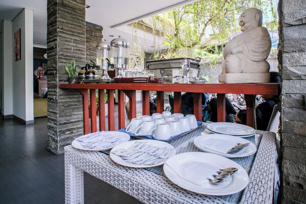 A dining area with a stone pillar, a Buddha statue, and a buffet setup with plates and cutlery.