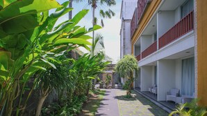 A narrow pathway flanked by lush greenery and a building with outdoor seating. - Kamini Legian Hotel (Kuta)
