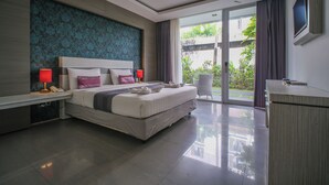 A modern hotel room with a large bed, a desk, and a view of greenery outside. - Kamini Legian Hotel (Kuta)
