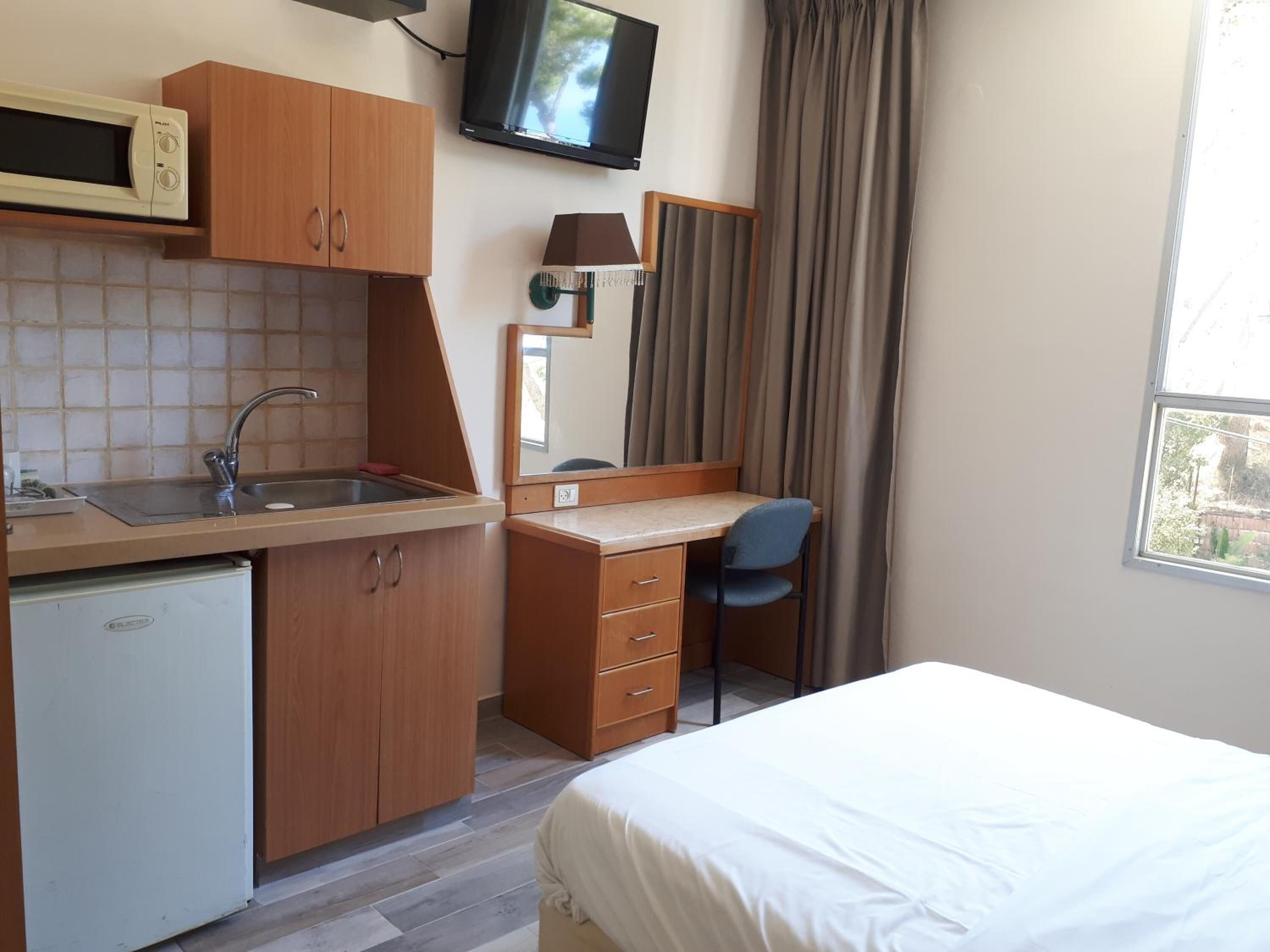 A compact hotel room with a kitchenette, a bed, a desk, and a TV.