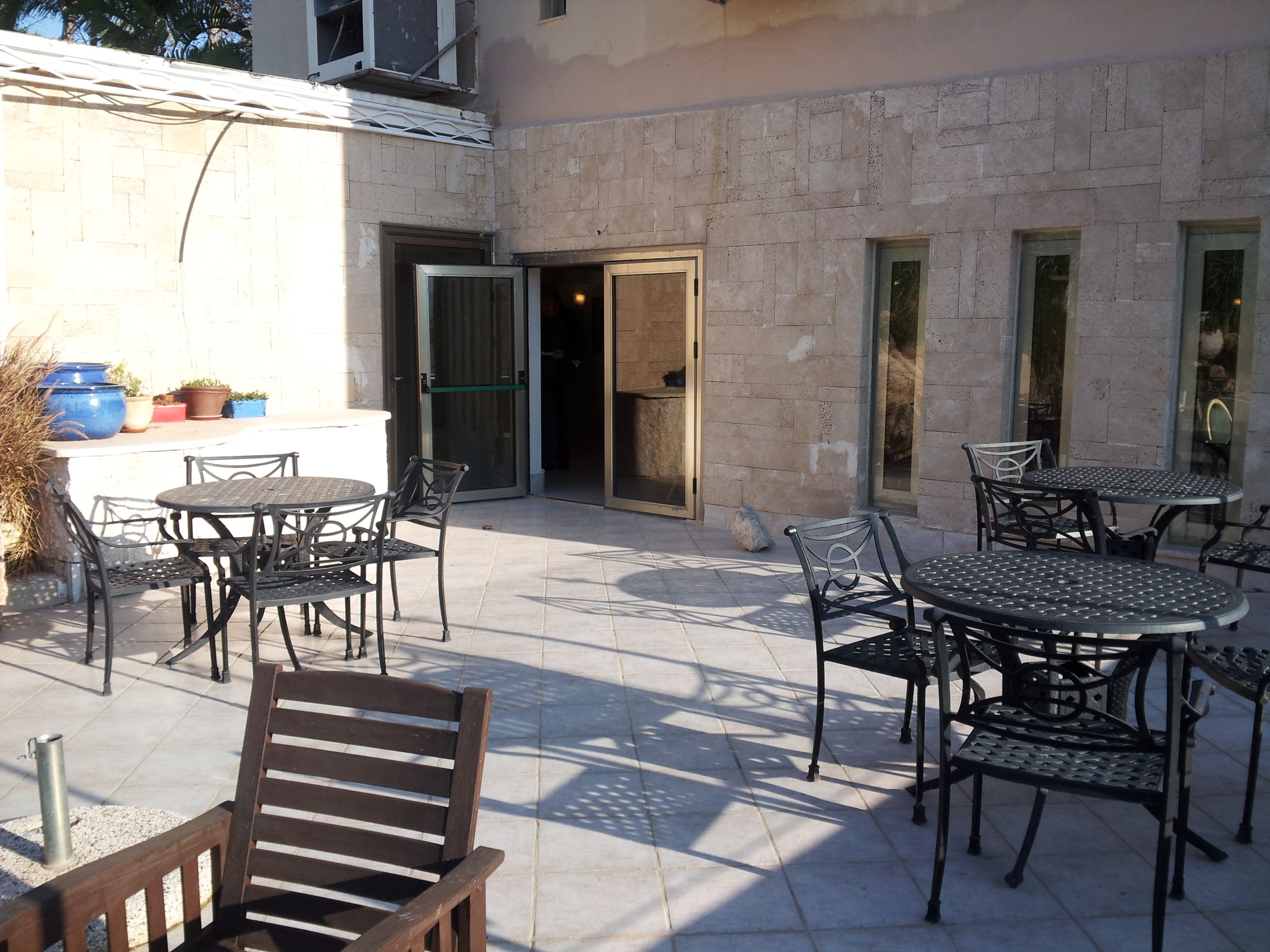 An outdoor patio area with multiple tables and chairs, a wooden bench, and a stone wall.
