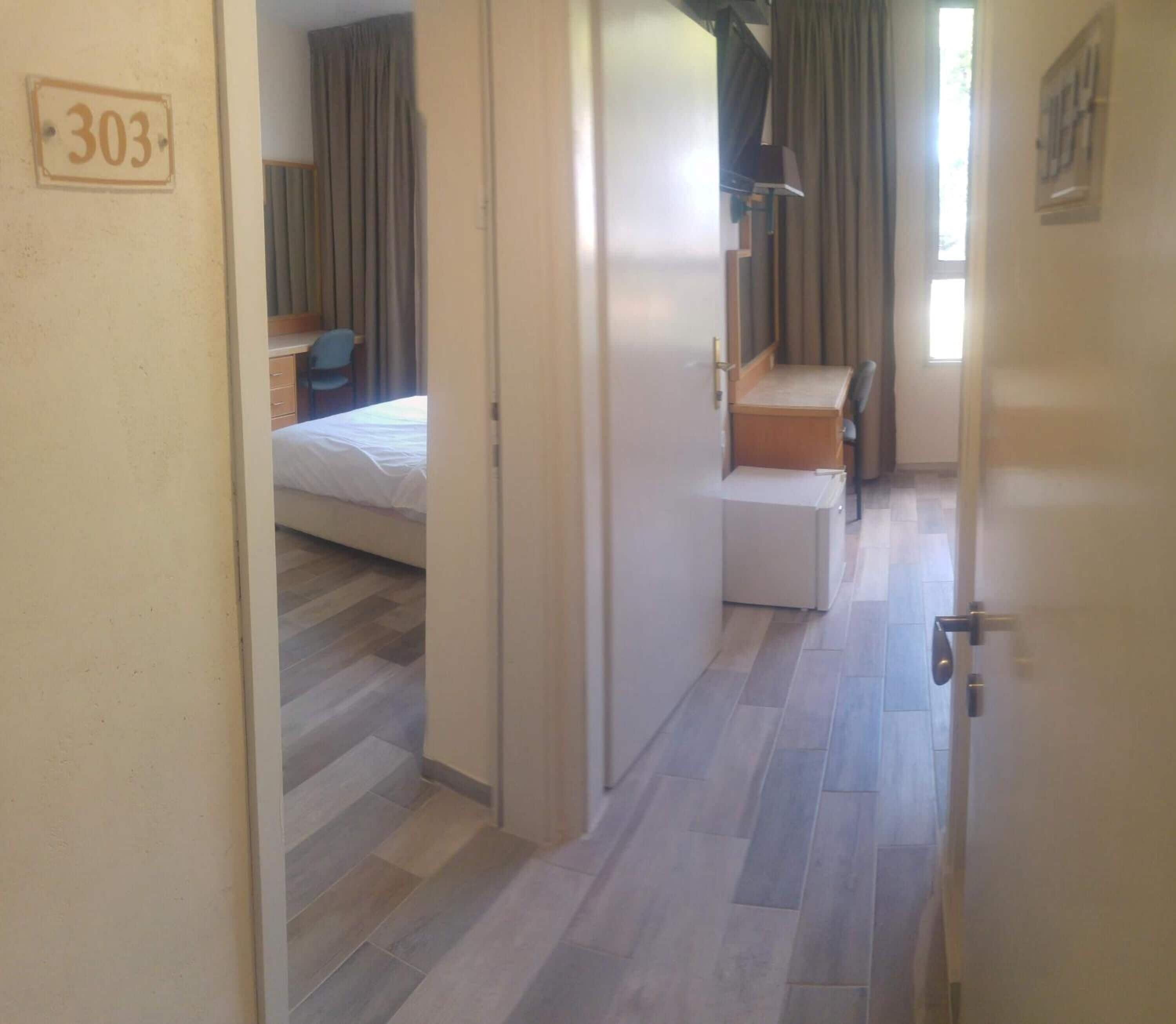 Una camera d'albergo con un letto, una scrivania e una sedia. Si vede una porta con il numero.