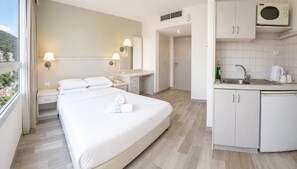 A hotel room with a bed, bedside table, lamp, and a view of the city. - Marom Residence Romema (Haifa)