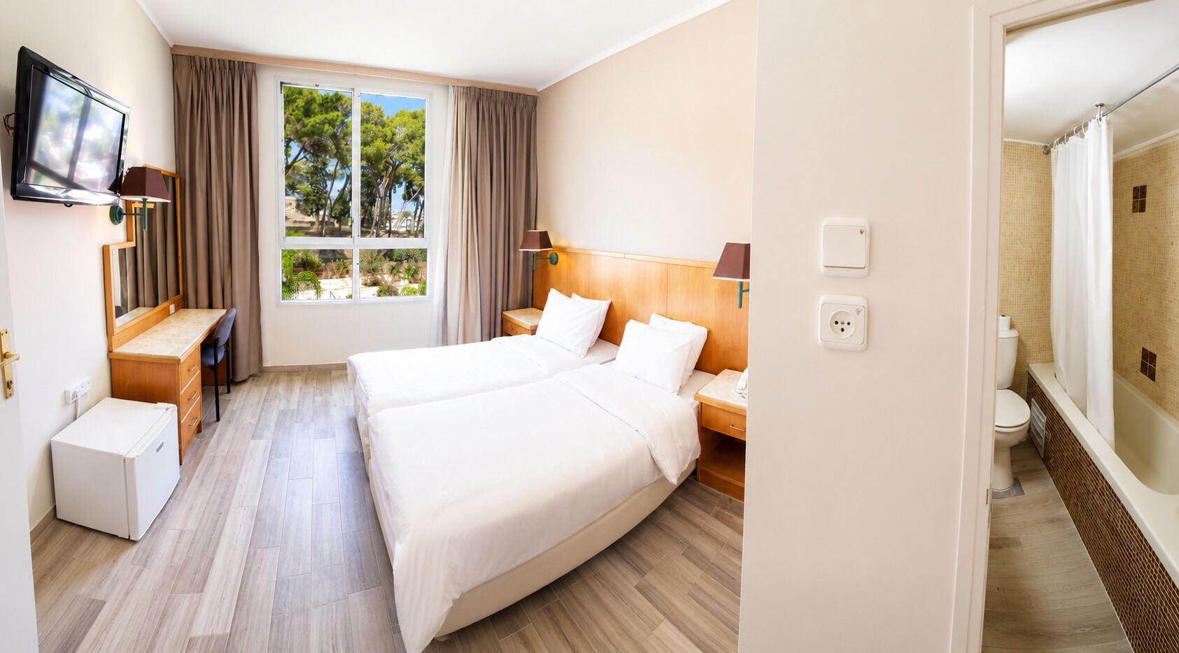 Ein Hotelzimmer mit zwei Betten, einem Schreibtisch, einem Sessel, einem Fernseher und einem Badezimmer mit Dusche und Toilette.