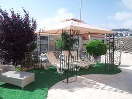 Terraza en la azotea con mobiliario exterior, zona cubierta y vistas a la ciudad.