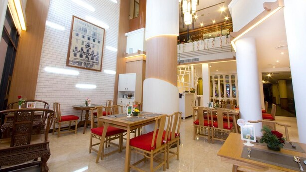 A hotel lobby with wooden furniture, red cushioned chairs, a large framed picture on the wall, and a staircase leading to an upper level. - Chinatown Hostel (Bangkok)
