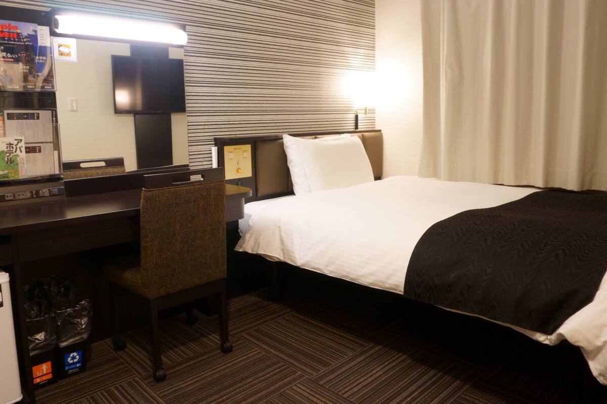 Una habitación de hotel con cama, escritorio, silla, espejo y televisor.