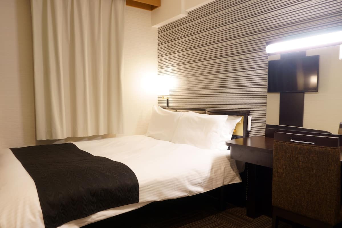Habitación de hotel con una cama, un escritorio, una silla y un televisor de pantalla plana.