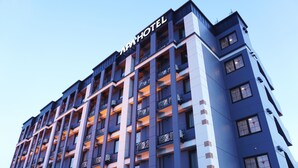 Een meerlaags hotel met een modern architectuurontwerp, met balkons op elke verdieping en een opvallend bord bovenaan.