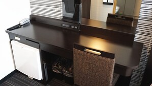 Een kleine hotelkamer met kitchenette, een kleine koelkast, een compacte wasmachine en een spiegel boven de wastafel.