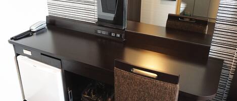 A compact hotel room with a kitchenette, a small refrigerator, a compact washer, and a mirror above the sink.