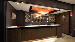 Een hotel receptie met een houten balie, een grote spiegel en een kroonluchter.