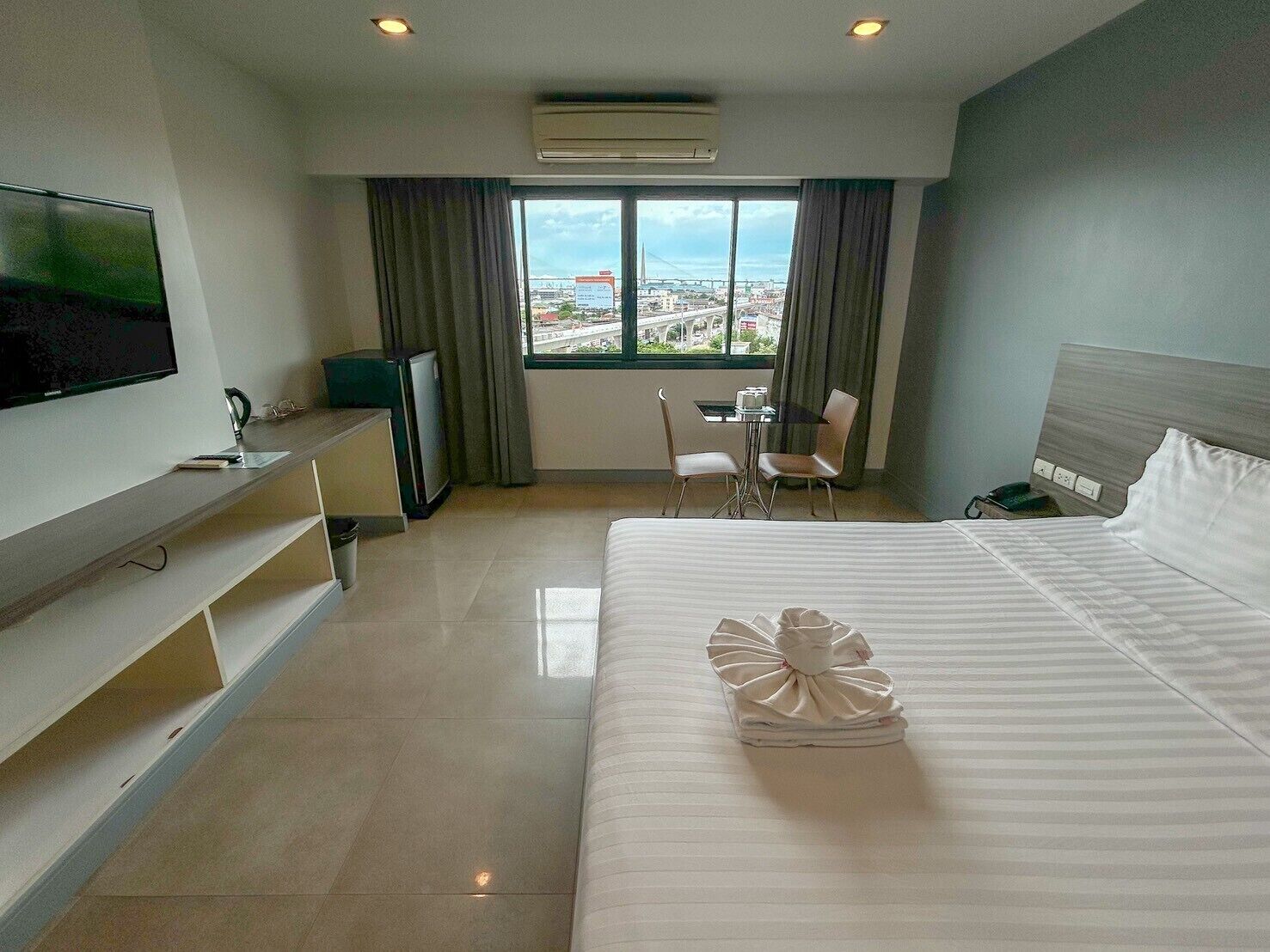 A hotel room with a large bed, a TV, a desk with a chair, and a window with a city view.