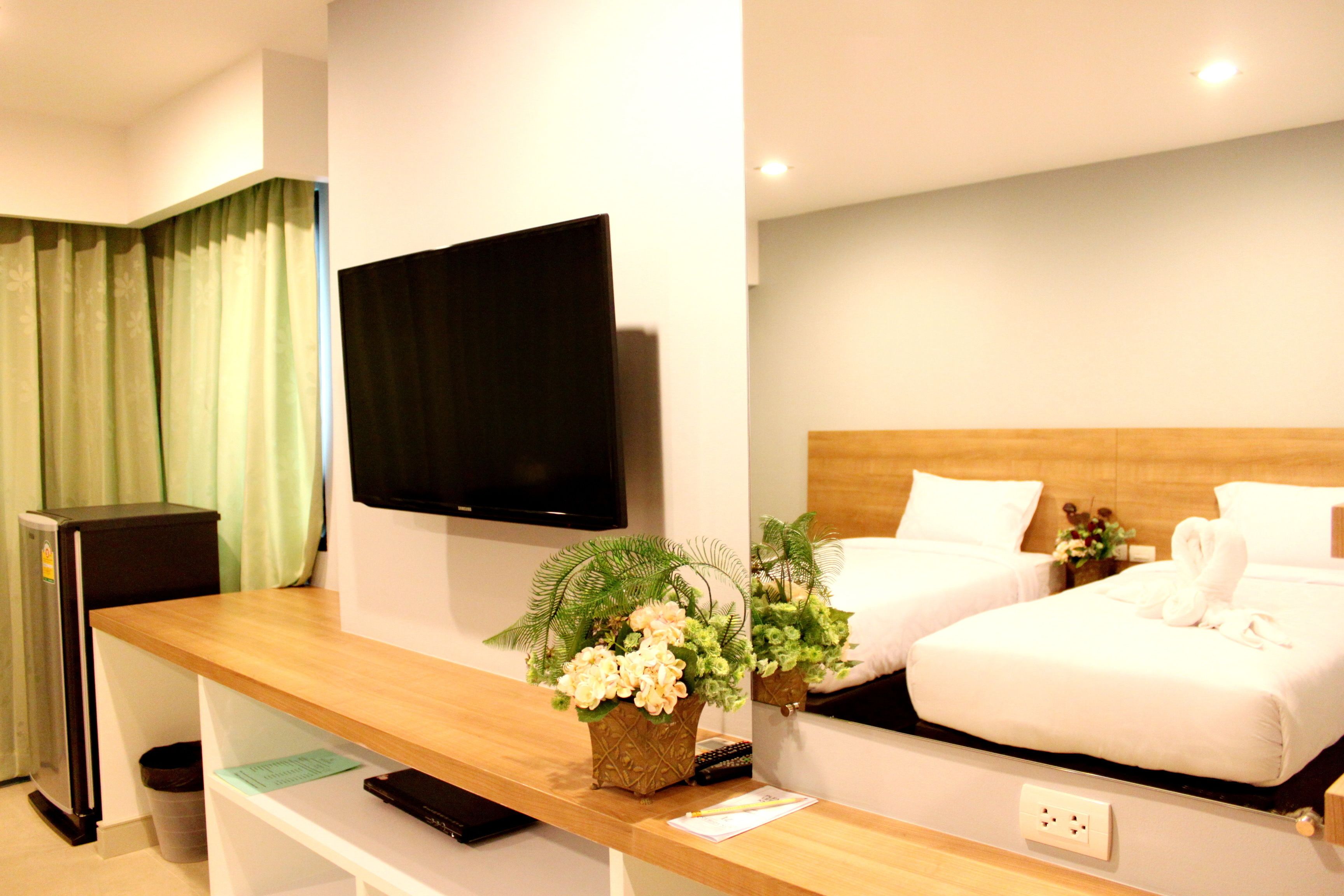 Habitación de hotel con un escritorio de madera, un televisor de pantalla plana, dos camas con ropa blanca y una pequeña planta en maceta.