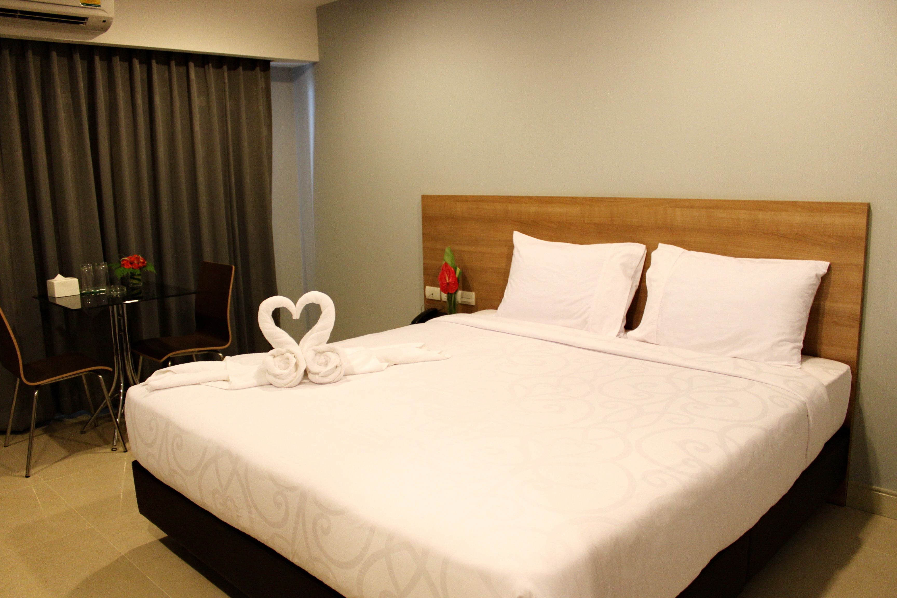 A hotel room with a neatly made bed, a wooden headboard, a small table with a vase of flowers, and a chair.