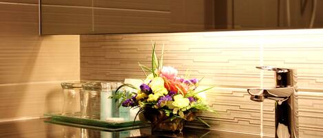 A modern kitchen with a stainless steel sink, a glass dish rack, and a decorative flower arrangement on the counter.