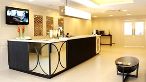 Un hall d’hôtel moderne avec un long comptoir d’accueil, un téléviseur à écran plat fixé au mur et une petite table ronde sur laquelle est posé un magazine.