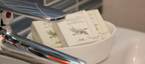 A white bowl containing several white soaps with green leaf designs, placed on a white surface. - Chrismare Hotel (Taormina)