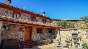 A stone building with a tiled roof, a wooden door, and a small outdoor seating area with a table and chairs. - Entre Valles (Carrocera)
