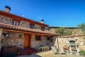 A stone building with a tiled roof, a wooden door, and a small outdoor seating area with a table and chairs. - Entre Valles (Carrocera)