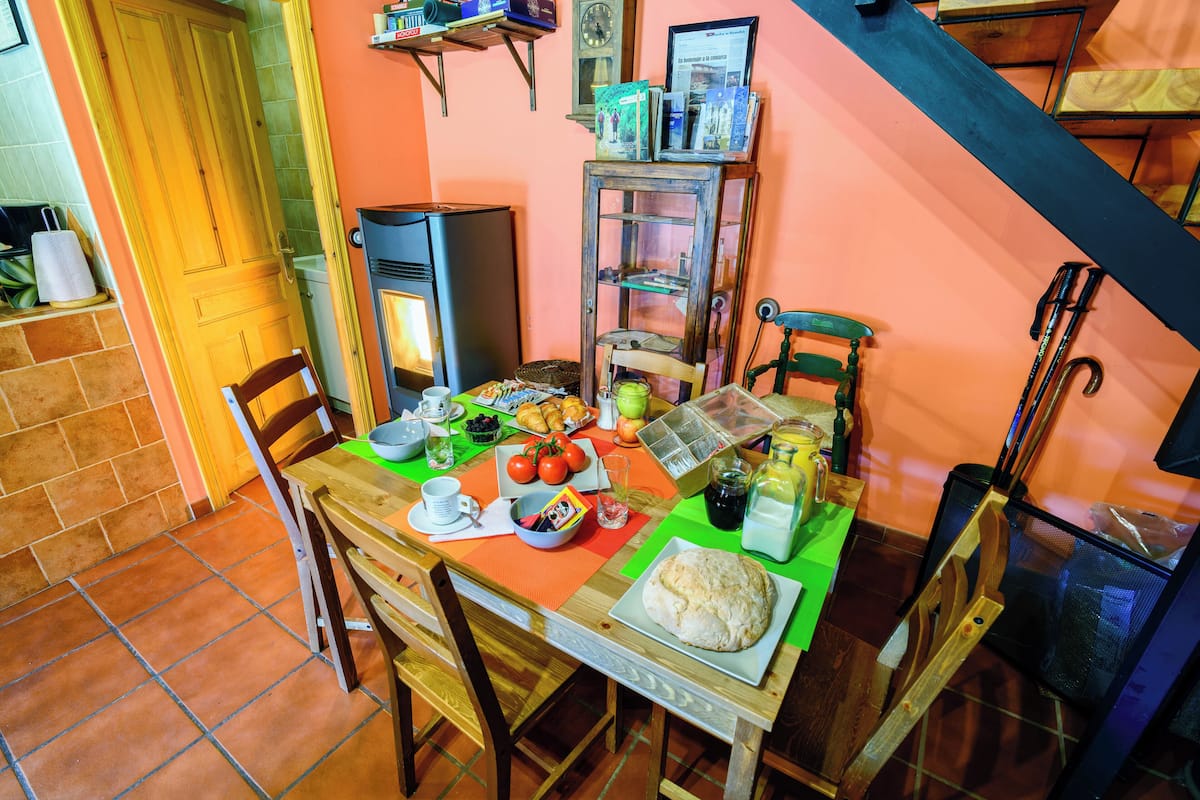 A dining area with a wooden table, chairs, and a variety of food items.