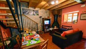 A cozy living room with a fireplace, a dining area with a table set for a meal, and a staircase leading to an upper level. - Entre Valles (Carrocera)