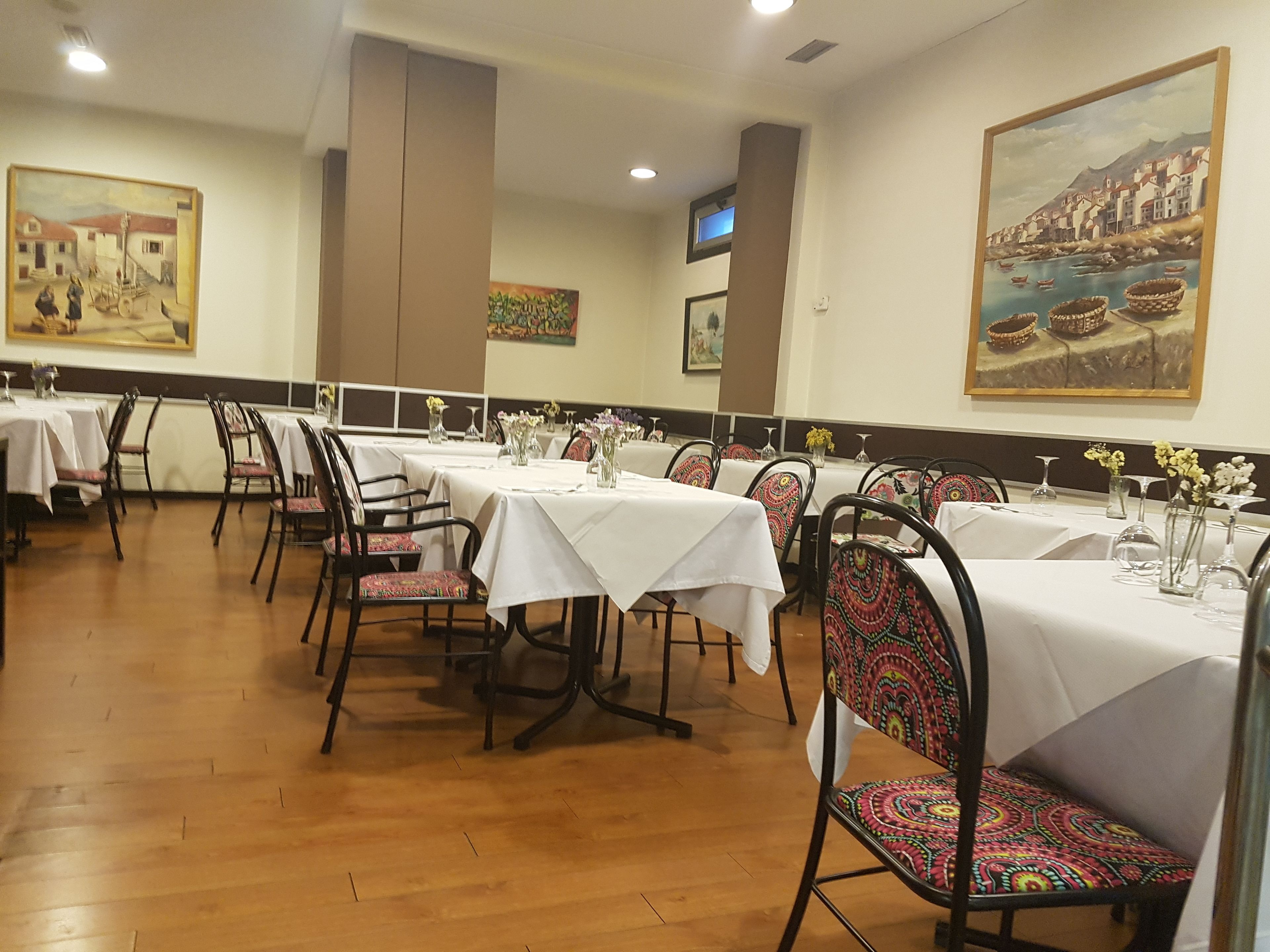 A dining area with multiple tables and chairs, each with a white tablecloth and vases of flowers.