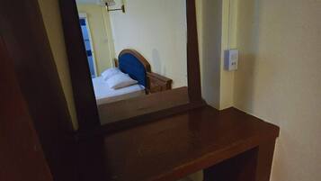 A wooden desk with a mirror, a small stool, and a bed with a blue headboard in the reflection.