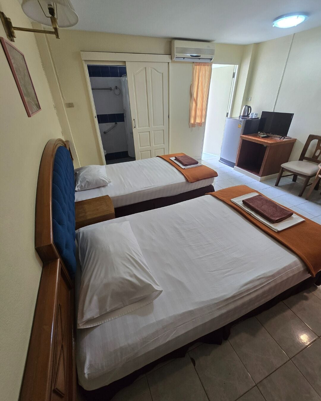 Ein Hotelzimmer mit zwei Betten, einem Schreibtisch, einem Fernseher und einem Kleiderschrank.
