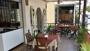 Um pátio de restaurante com chão de azulejos, mobiliário de madeira e vista para a rua.