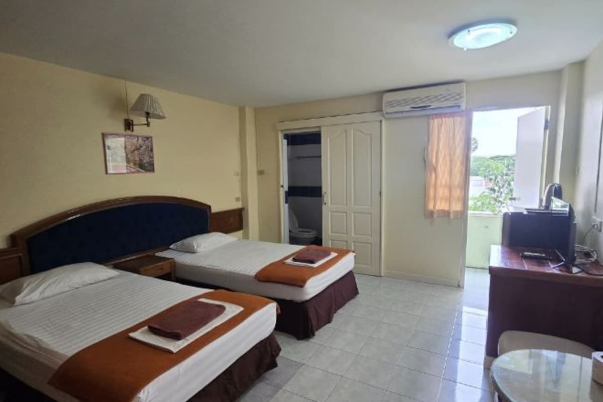 A hotel room with two beds, a desk with a computer, and a view of the outside.