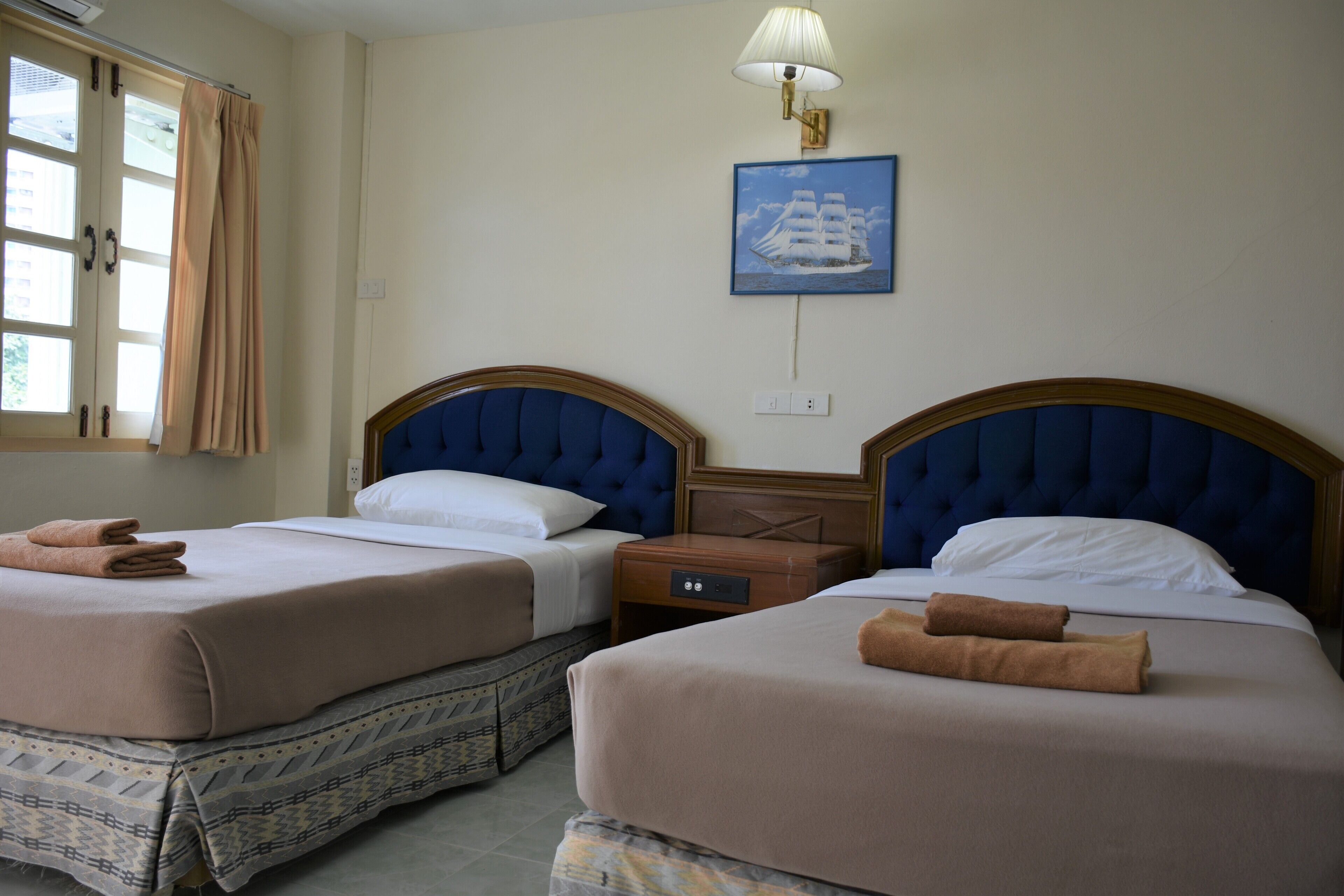 A hotel room with two beds, each with a headboard, a nightstand, and a lamp.